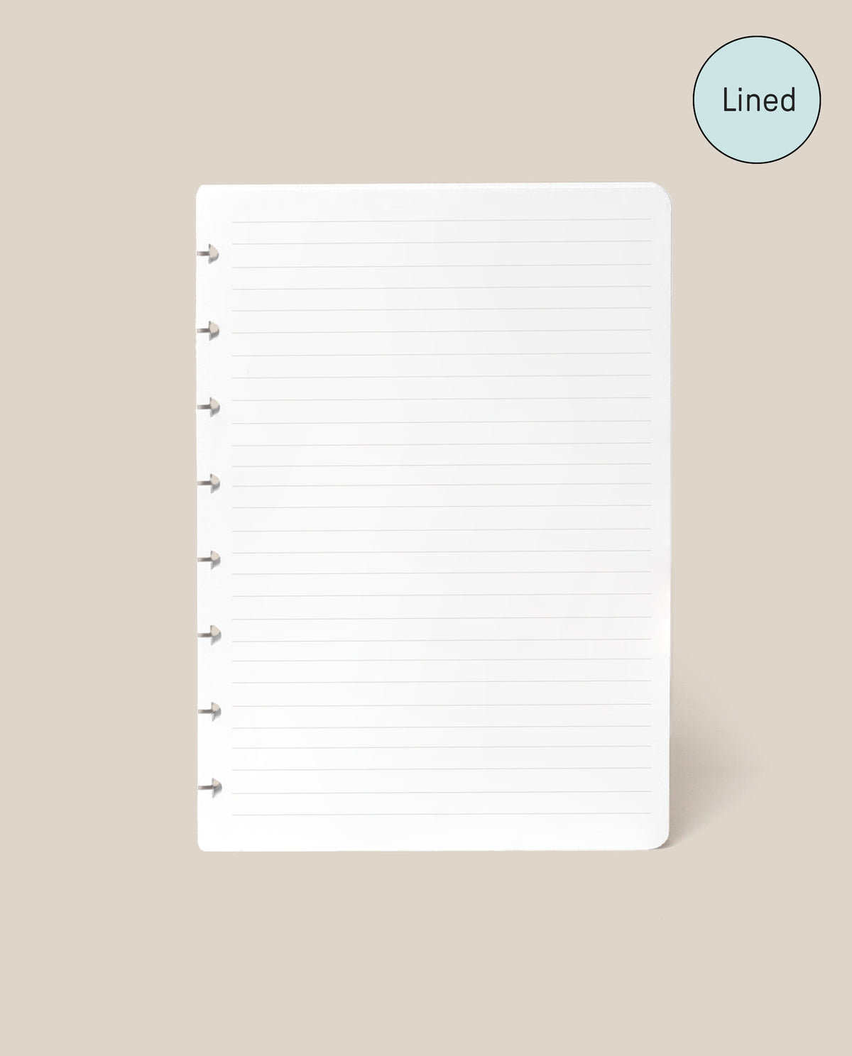 A Discbound Journal Refill - Lined (Standard 6″ x 8.5″) page, featuring white paper with disc-bound holes along the left edge and neat lines, is centered on a beige background. Designed as refill paper for your Heirloom Discbound Journal, each page includes a blue circle in the top right corner labeled “Lined.”.