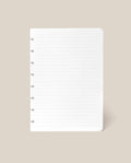 A single sheet from the Discbound Journal Refill - Lined (Standard 6″ x 8.5″), featuring white, lined paper with punched holes on the left side, displayed on a beige background—ideal for replenishing your Heirloom Discbound Journal.