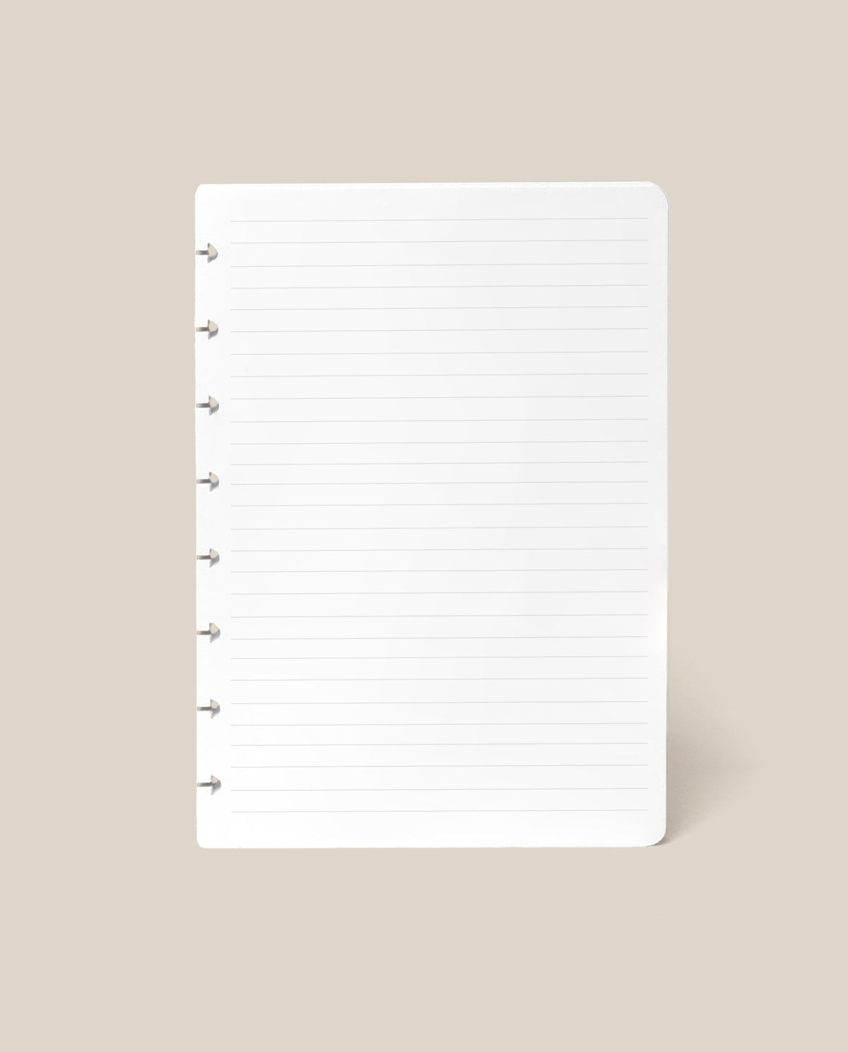 A single sheet from the Discbound Journal Refill - Lined (Standard 6″ x 8.5″), featuring white, lined paper with punched holes on the left side, displayed on a beige background—ideal for replenishing your Heirloom Discbound Journal.