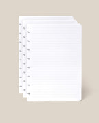 Four overlapping sheets of the Discbound Journal Refill - Lined (Standard 6″ x 8.5″)—white, lined pages with holes along the left edge, perfect for your Heirloom Discbound Journal—set against a plain beige background.