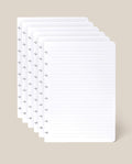 Six sheets of the Discbound Journal Refill - Lined (Standard 6″ x 8.5″), each with neatly lined pages and discbound punched holes along the left edge, are stacked against a light beige background—perfect for adding to your Heirloom Discbound Journal.