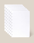 Six sheets of the Discbound Journal Refill - Lined (Standard 6″ x 8.5″), each with neatly lined pages and discbound punched holes along the left edge, are stacked against a light beige background—perfect for adding to your Heirloom Discbound Journal.