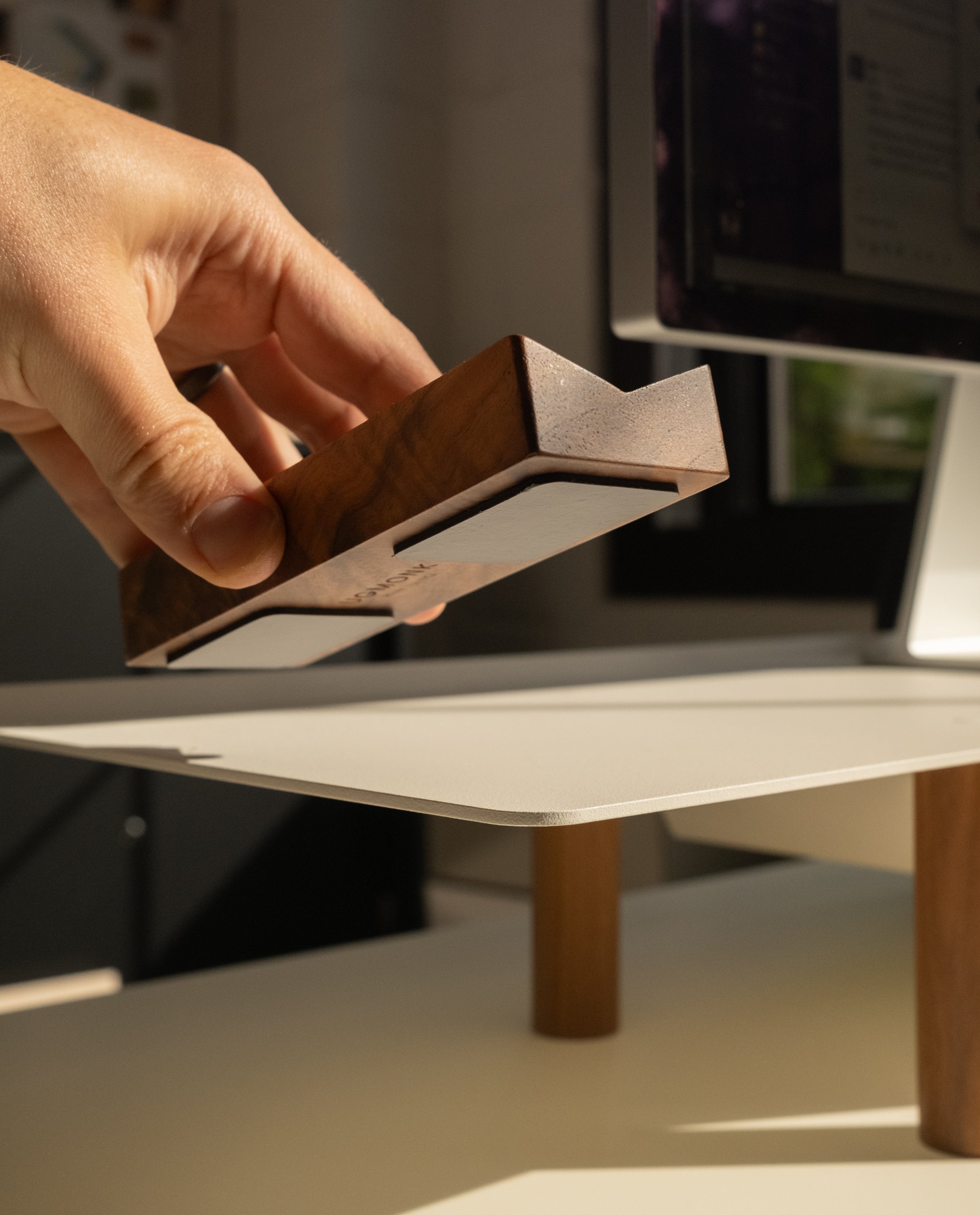 A hand places the Magnet Kit (Pen Tray and Analog Weekly) onto a light-colored desk with wooden legs, with a computer monitor visible in the background.