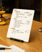 An Analog Starter Kit (Black) sits upright on a wooden desk, held by its sleek aluminum card stand labeled Analog. The DAY 2 notecard displays orange and black handwritten notes, sketches, and checklists—reminiscent of a paper card system or task cards. Other office items and papers are nearby.