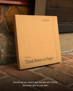 A brown Analog Starter Kit (Silver) box labeled Think Better on Paper leans against a stone wall on a brick surface. Text below reads, Everything you need to get started with the paper card system and task cards. Delivered right to your door.