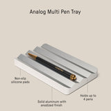 The Analog Multi Pen Tray (Silver Aluminum) features a solid anodized aluminum build, non-slip silicone pads, and holds up to 4 pens. Dimensions: 5.77" x 3.35" x 0.62". Shown with one black and gold pen resting on the tray.