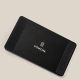 The Analog Multi Pen Tray (Black Aluminum) is a black rectangular solid aluminum desk organizer with rounded corners, the UGMonk logo and name in white at the center, and black rubber pads on two ends, shown on a light beige background.