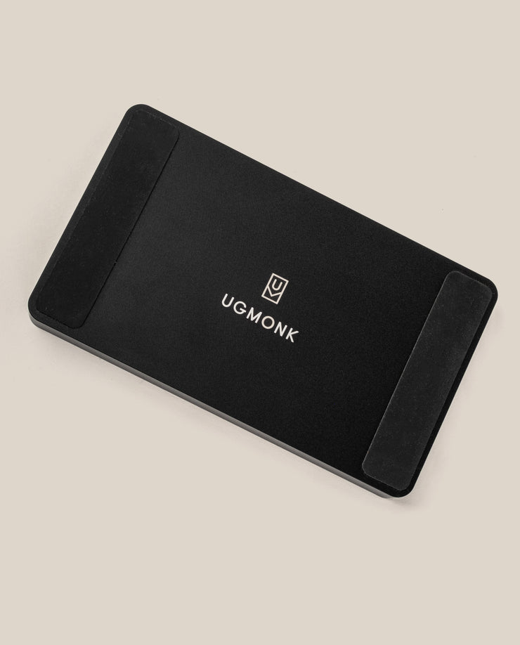 The Analog Multi Pen Tray (Black Aluminum) is a black rectangular solid aluminum desk organizer with rounded corners, the UGMonk logo and name in white at the center, and black rubber pads on two ends, shown on a light beige background.