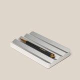 A black and gold pen with UGMONK branding rests on the Analog Multi Pen Tray (Silver Aluminum) against a light beige background.