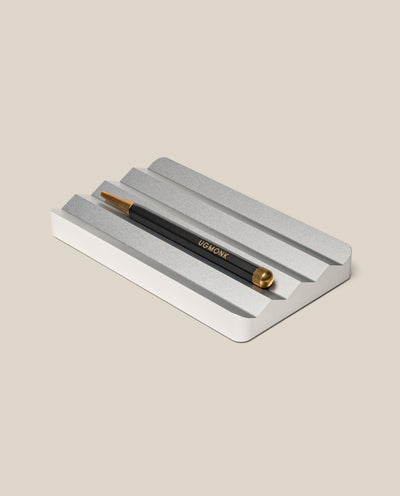 A black and gold pen with UGMONK branding rests on the Analog Multi Pen Tray (Silver Aluminum) against a light beige background.