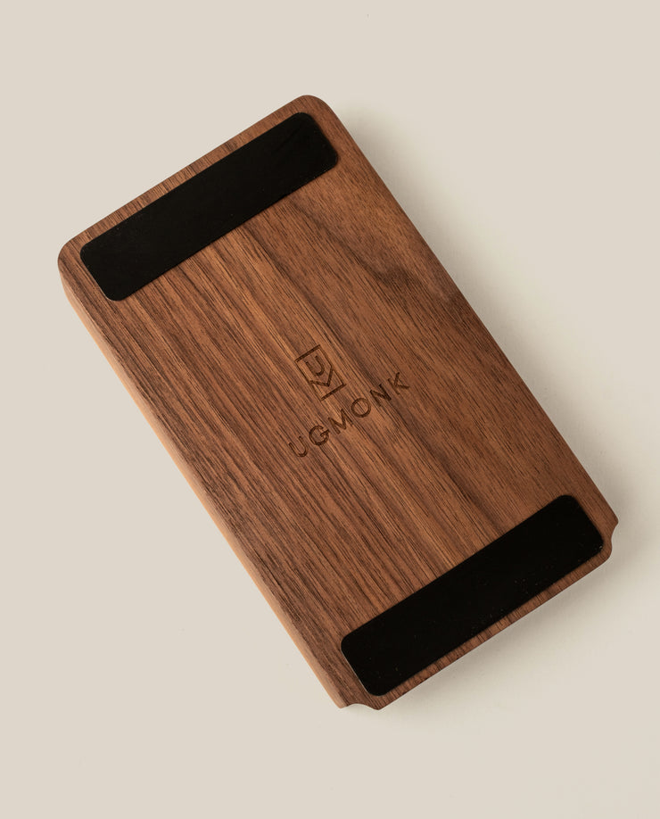 A rectangular walnut Analog Annual Kit with two black strips at the top and bottom, engraved with the Ugmonk logo and name in the center, photographed on a light beige background.