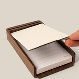 A hand lifts a lined notepad sheet from the Analog Annual Kit (Walnut), a wooden desk organizer designed as a Daily and Weekly Card Holder with checkboxes and lines for notes or tasks.