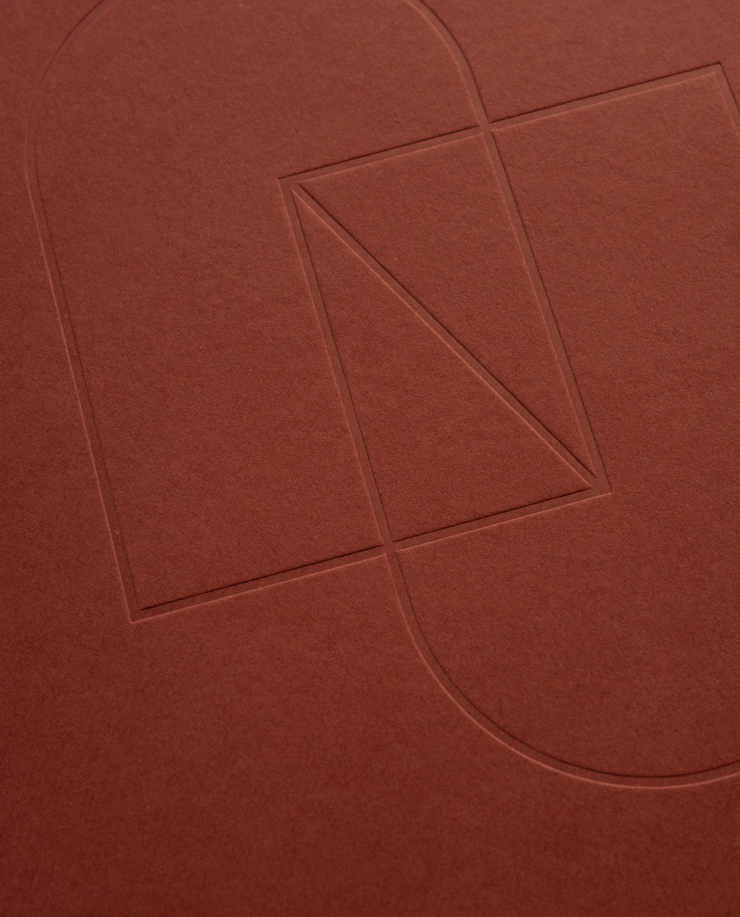 Embossed geometric shapes—a rectangle, triangle, and two semicircles—are outlined on the textured cover of the maroon Layflat Notebook.