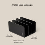 The Analog Card Organizer (Black Aluminum) is a three-slot card tray with non-slip silicone pads, made from solid anodized aluminum. It fits all card sizes and measures 5.77 x 3.35 x 0.62 inches.