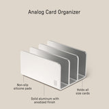 The Analog Card Organizer (Silver Aluminum) is a sleek organizer with three slots, crafted from anodized solid aluminum. It features non-slip silicone pads, ample card storage, and measures 5.77 x 3.35 x 0.62 inches.