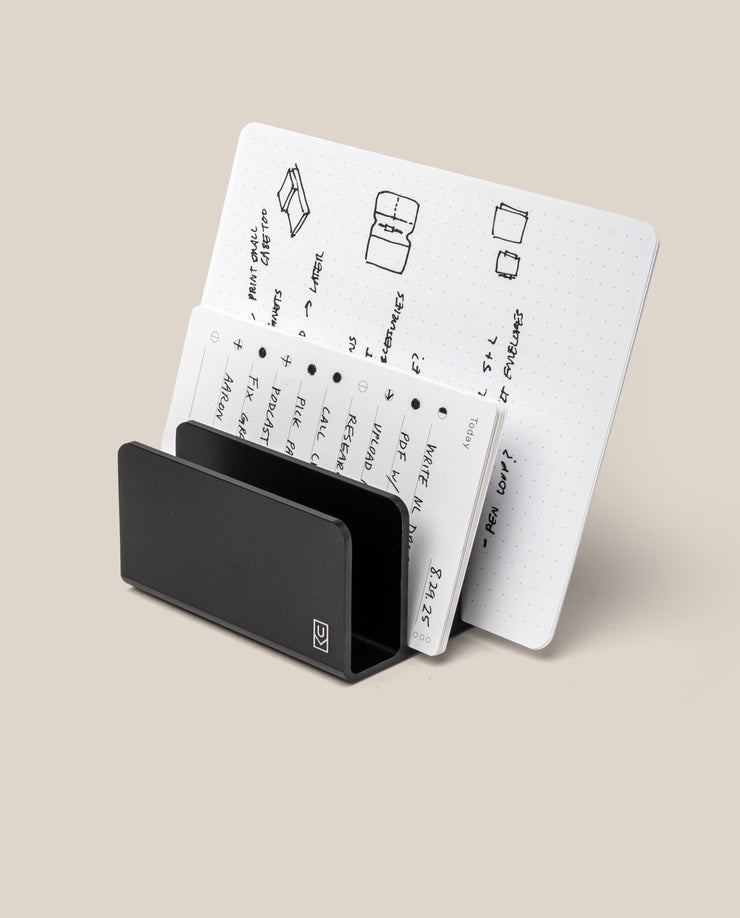 The Analog Card Organizer (Black Aluminum) displays multiple white cards with handwritten notes, diagrams, and sketches arranged in rows against a plain beige background.