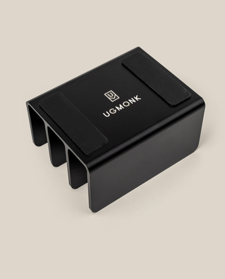 The Complete Analog Collection (Black Aluminum): a black, rectangular metal desktop organizer with three slots, two anti-slip pads on top, and a white UGMONK logo, shown against a light beige background.