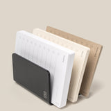 The Complete Analog Collection (Black Aluminum): a black desktop organizer with three notepads—white, cream, and brown—for weekly planning in a horizontal layout, shown against a neutral beige background.