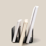 The Analog Card Organizer (Black Aluminum) holds three notebooks of varying sizes upright against a neutral beige background, arranged from smallest to largest with their covers and pages visible side-on.