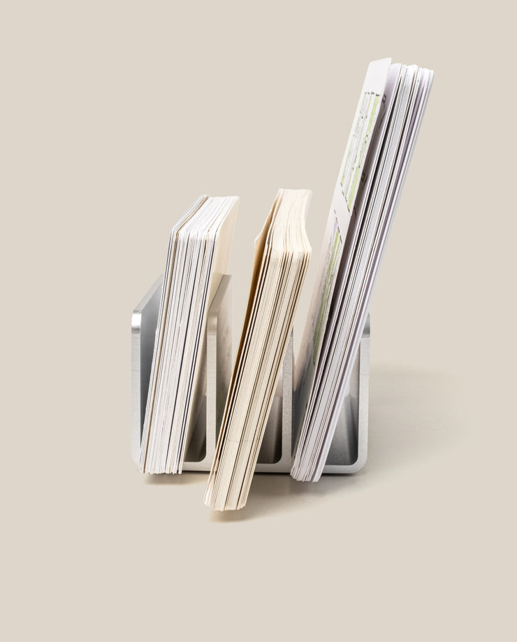 Three The Complete Analog Collection (Silver Aluminum) desktop organizers hold varying stacks of paper upright against a light beige background; each stack differs in height and thickness.