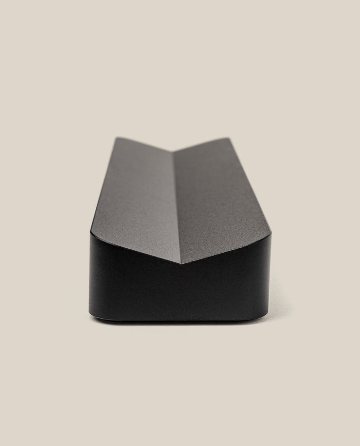 The Analog Pen Tray (Black Aluminum) features a sleek, angular design with a central crease, ideal as a modern desk organizer. Shown on a plain, light beige background, its minimalist style complements any workspace.