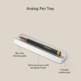 The Analog Pen Tray (Silver Aluminum) is a sleek, anodized solid aluminum desk accessory with non-slip pads and a V-shaped groove to secure your pen. Holds a black and gold pen. Dimensions: 5.77 x 1.33 x .62 inches.