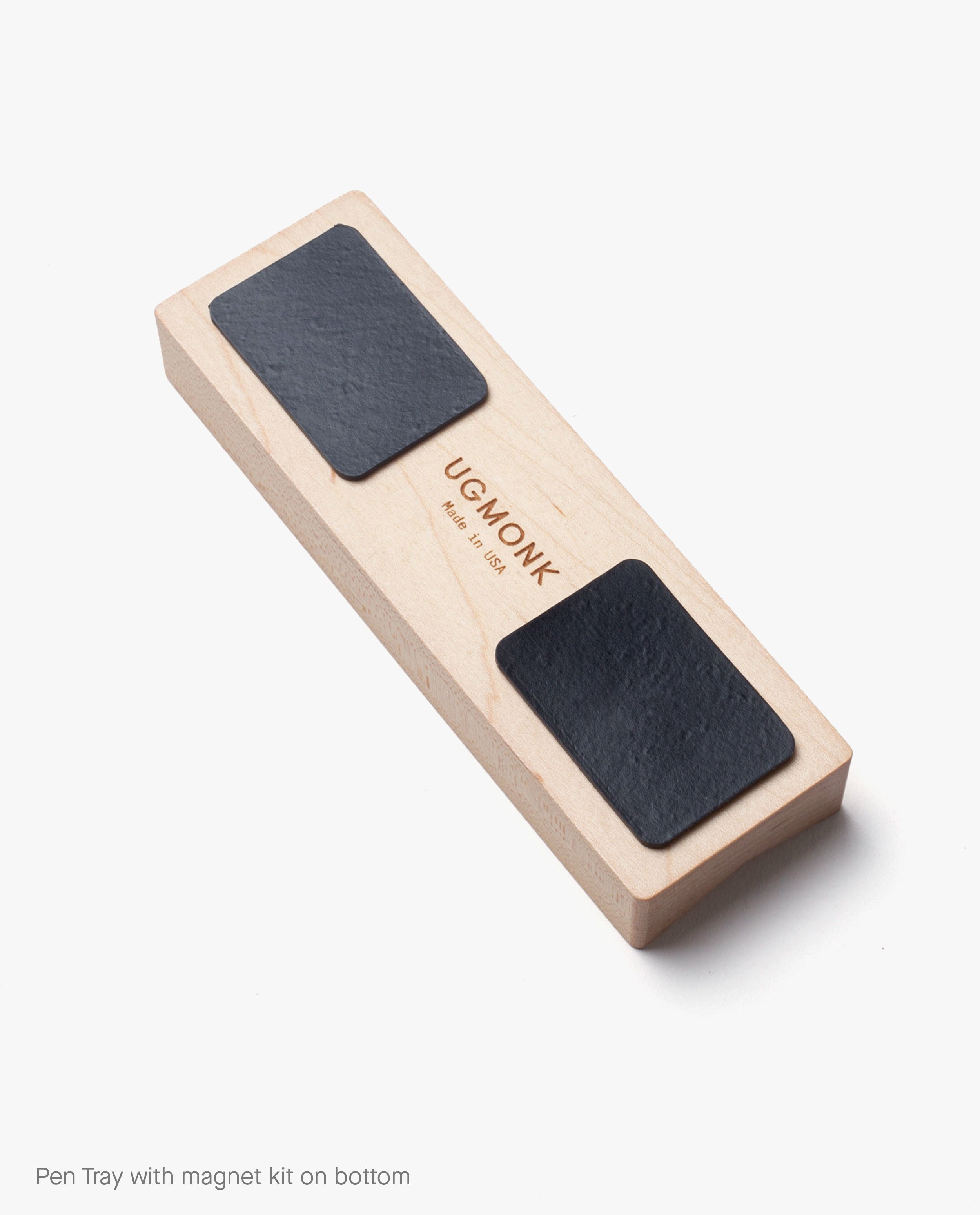 Magnet Kit (Pen Tray and Analog Weekly) features a rectangular wooden pen tray with two black rectangular magnets on the bottom, designed to complement the Gather Monitor Stand, and engraved with UGMONK branding on the top surface. The tray is shown resting on a white background.