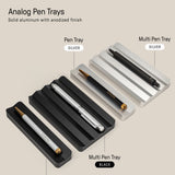 The Analog Multi Pen Tray (Black Aluminum) is shown as a sleek desk organizer. It holds multiple pens and features labels for color and tray type, all displayed on a beige background.
