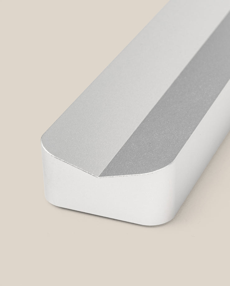 A close-up of the Analog Pen Tray in silver aluminum—a sleek, rectangular tray with a beveled edge—crafted from solid aluminum and displayed on a beige background.