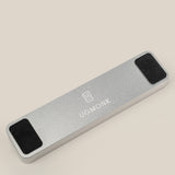 The Analog Pen Tray (Silver Aluminum) is a solid aluminum rectangular pen tray with UGMONK branding and logo on top, two black rectangular pads on each end, displayed on a light beige background—a sleek desk accessory.