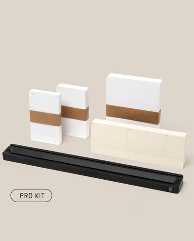 The Analog Card Bar - Pro Kit (Black) features note pads, sticky notes, Task Cards, and a sleek black tray, all neatly arranged on a beige background. "PRO KIT" appears in a rounded rectangle at the bottom left.