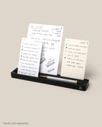 The Analog Card Bar (Small 10" - Black) is a solid aluminum desk organizer that neatly holds a pen and three upright notecards in display slots. A caption reads, “*Cards sold separately.”.