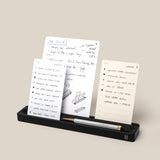 The Analog Card Bar (Small 10" - Black) is a solid aluminum desk organizer that neatly holds a pen and three upright notecards in display slots. A caption reads, “*Cards sold separately.”.