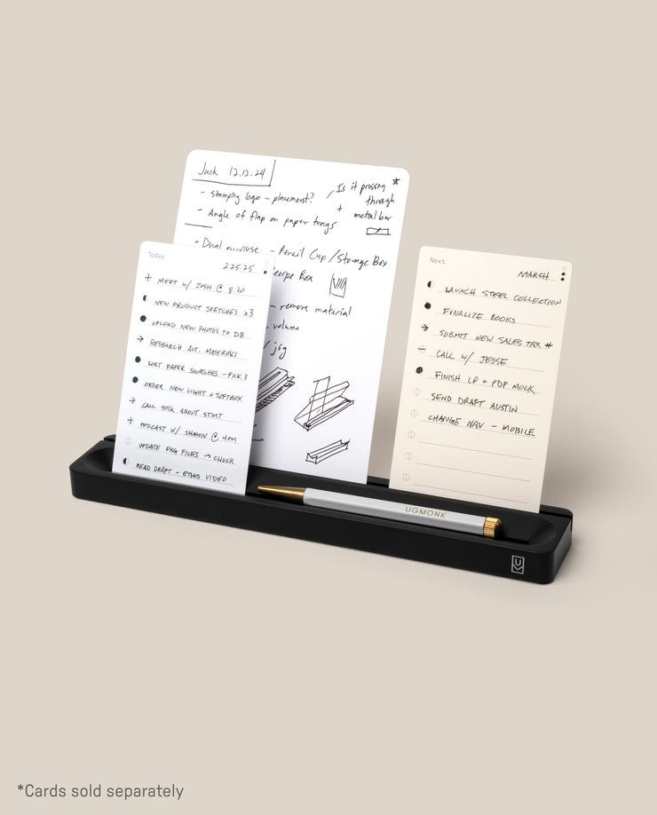 The Analog Card Bar (Small 10" - Black) is a solid aluminum desk organizer that neatly holds a pen and three upright notecards in display slots. A caption reads, “*Cards sold separately.”.