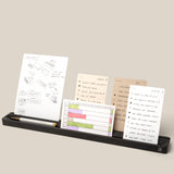 The Analog Card Bar (Large 16" – Black), a solid aluminum desk organizer tray, holds a pencil and four note cards with sketches and notes on a light beige background. Text at bottom: “*Cards sold separately.”.
