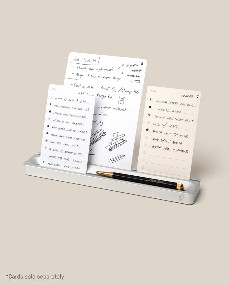 The Analog Card Bar (Small 10" - Silver) stylishly displays three white notecards with handwritten ideas. A black and gold pen sits in front, serving as a sleek pen tray. Text reads: *Cards sold separately.