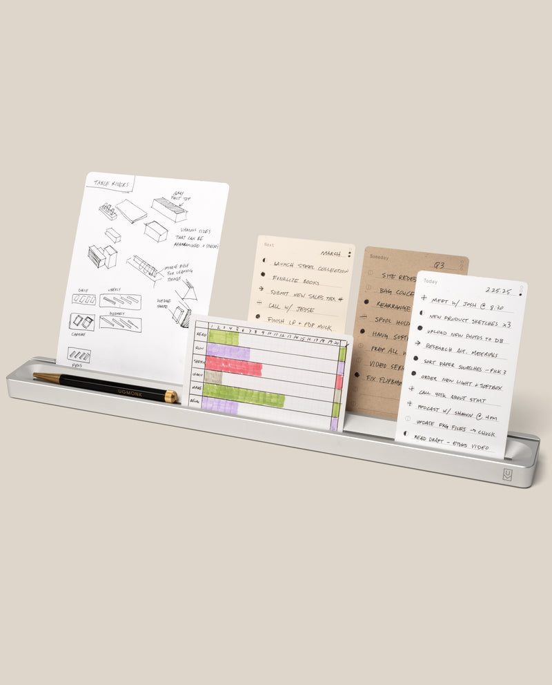 The Analog Card Bar (Large 16" – Silver) is a slim solid aluminum desk organizer that holds a pen and several task cards with handwritten notes, sketches, and lists, all neatly arranged against a beige background.
