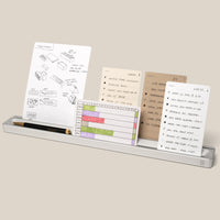 The Analog Card Bar (Large 16" – Silver) is a minimalist solid aluminum desk organizer that holds several task cards featuring sketches, lists, and charts, as well as a black pen and gold pencil. *Cards sold separately.
