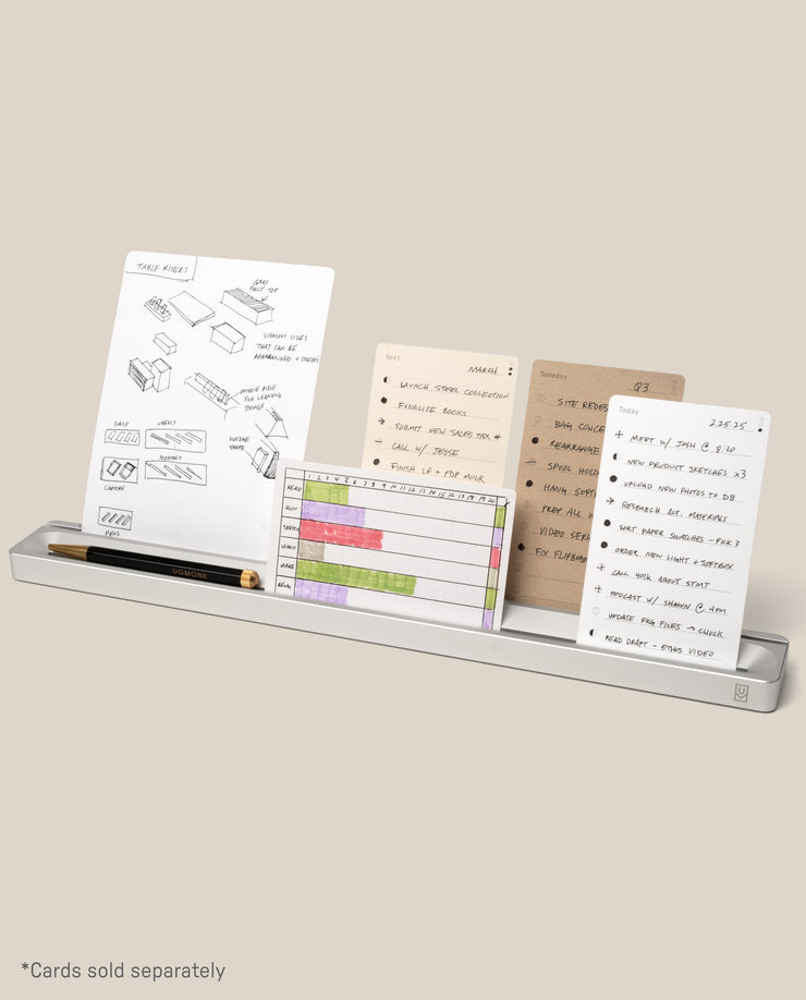 The Analog Card Bar (Large 16" – Silver) is a minimalist solid aluminum desk organizer that holds several task cards featuring sketches, lists, and charts, as well as a black pen and gold pencil. *Cards sold separately.