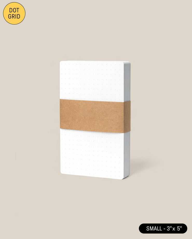 A pack of Analog Dot Grid Cards - Small (1-Pack), neatly stacked 3x5 and wrapped with a brown paper band, displayed against a light beige background.