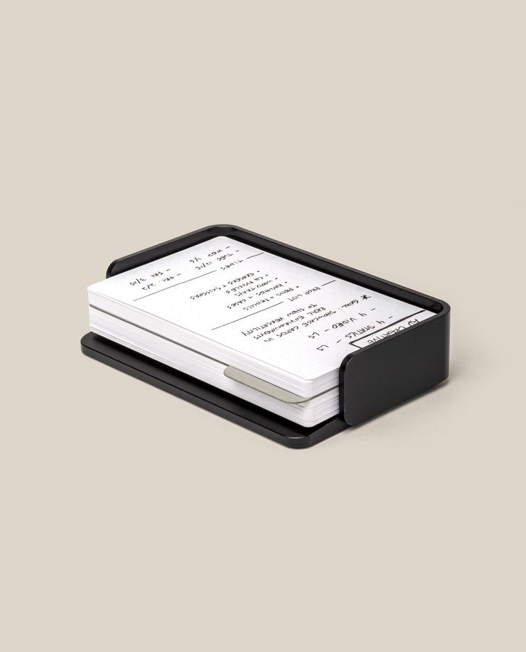 The Analog Capture Kit - Small (Black Aluminum) features a black rectangular card holder, ideal for organizing your Small Dot Grid Cards, containing white index cards with handwritten notes on a light beige surface.