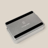 The Analog Capture Kit - Small (Silver Aluminum), a rectangular tray with rounded edges and black grooves, displays the white UGMONK logo on its lid and rests on a light beige surface—ideal for organizing your Small Dot Grid Cards.