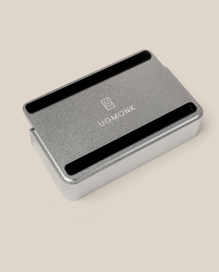 The Analog Capture Kit - Small (Silver Aluminum), a rectangular tray with rounded edges and black grooves, displays the white UGMONK logo on its lid and rests on a light beige surface—ideal for organizing your Small Dot Grid Cards.