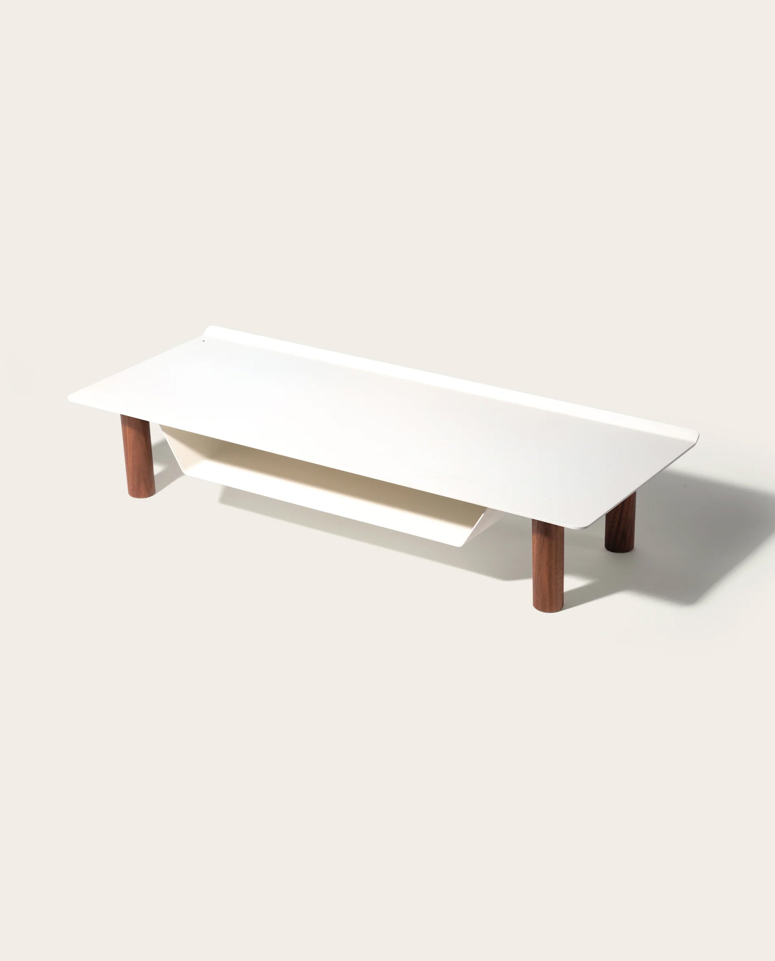 The Gather Small Monitor Stand (White/Walnut) features a minimalist white top with rounded corners, four cylindrical walnut legs, and a slanted lower shelf—ideal as a space-saving desk organizer.