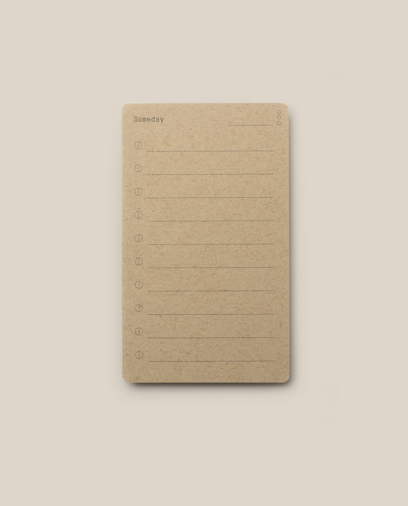 A brown notepad inspired by the Analog - Someday Cards, featuring “Someday” printed at the top. Each page offers ten numbered lines for writing and a blank space for the date in the upper right corner—perfect for creative goal setting. The notepad is centered on a light beige background.