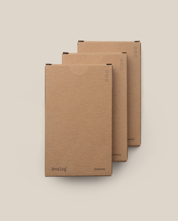 Three brown cardboard boxes of Analog - Someday Cards (3-Pack) are stacked in a staggered arrangement on a light beige background, featuring uncoated writing cards for versatile organization.