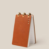 Small brown leather notepad with gold accents on a beige background