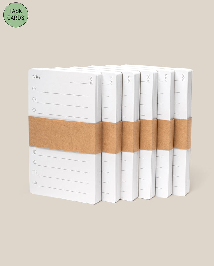 Six stacks of Analog - Task Cards (6-Pack), each with "Today" and lines printed, wrapped in brown paper bands, are arranged in a row on a beige background. A green circle in the corner displays "Task Cards.