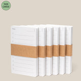 Six stacks of white Analog - Task Cards, each with numbered lines and wrapped in a brown band, are displayed on a light beige background. A green label in the corner reads “TASK CARDS”—ideal for your productivity system.
