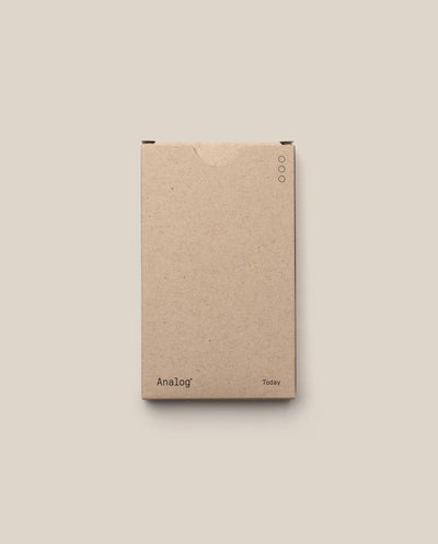 A plain brown cardboard box labeled "Analog" (lower left) and "Today" (lower right), with three circles near the top right, contains Analog - Today Cards (1-Pack) for prioritizing tasks, shown against a beige background.